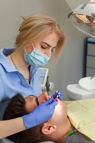 Мужчина посещает дантистку в клинике. Молодой человек сидит рот широко открыт в офисе стоматолога на ежегодном осмотре. Девушка-доктор
