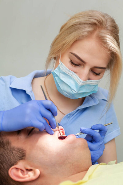 Мужчина посещает дантистку в клинике. Молодой человек сидит рот широко открыт в офисе стоматолога на ежегодном осмотре. Девушка-доктор
