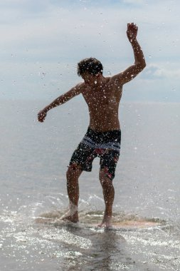 Genç bir adam sahilde skimboard üzerinde silüeti. su damlaları ve odak ön planda su sıçramalarına