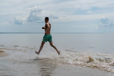 su ve kıyı boyunca şortlu genç bir adam çalışır