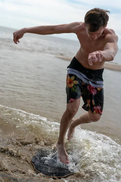 Genç bir adam için su sporları ile skimboarding sığ suda kıyıda gider