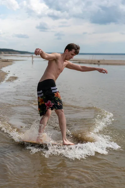 üzerinde bir skimboard sahilde su sporları için genç bir adam giriyor