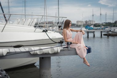 Elbiseli bir kız bir iskele yat bir arka plan üzerine oturur