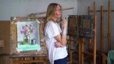 Şövale bir tablo ile karşı bir genç çekici sanatçı onun elinde bir fırça ve boya bir yüz ile standları.