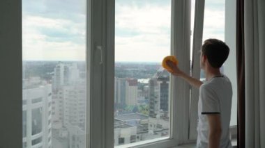 Bir adam şehre bakan bir pencereyı yıkıyor..