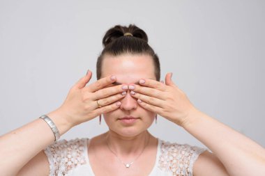 Gri arka planda bir kadın elleriyle gözlerini kapatıyor.