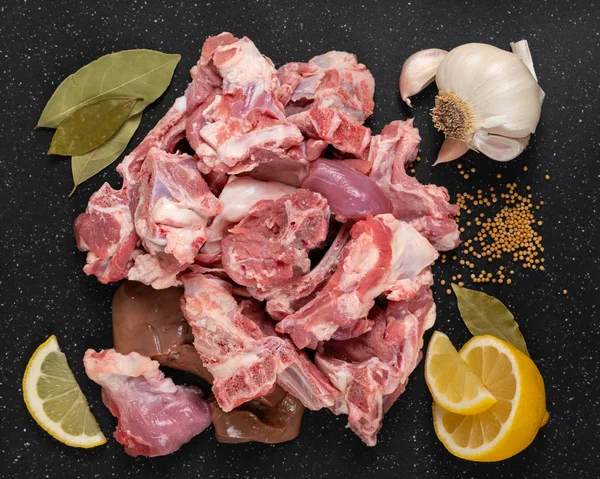 Taze çiğ keçi et güveç gibi siyah kesme tahtası baharat (hardal tohumu, sarımsak, limon ve defne yaprakları ile kesim).