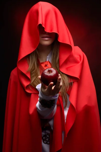 beautiful woman with red cloak holding red apple in studio