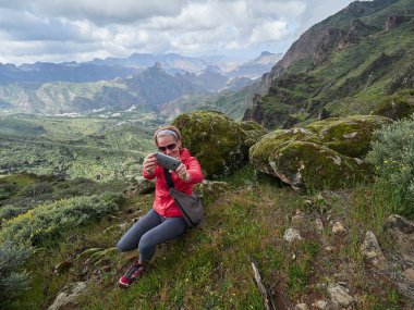 Genç kadın turist Cliff'in kenar ve çekici fotoğraflar üzerinde oturan sırt çantası ile