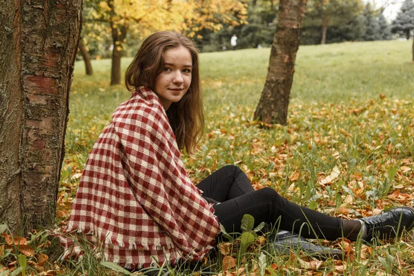 A girl is sitting next to a tree in autumn — Stock Photo, Image