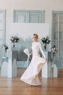 Çiçek ve dekorla düğün kemerinin önünde güzel bir gelin. Buket ellerde ve detaylarda. Kız mutlu, gülümsüyor ve dans ediyor. Modern tarzda bir gelinlik hayal et.