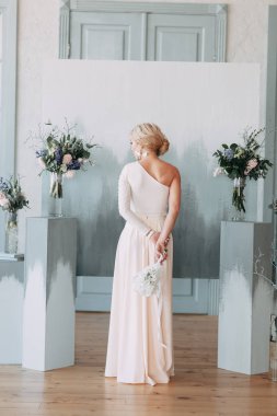 Çiçek ve dekorla düğün kemerinin önünde güzel bir gelin. Buket ellerde ve detaylarda. Kız mutlu, gülümsüyor ve dans ediyor. Modern tarzda bir gelinlik hayal et.