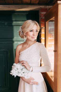 Çiçek ve dekorla düğün kemerinin önünde güzel bir gelin. Buket ellerde ve detaylarda. Kız mutlu, gülümsüyor ve dans ediyor. Modern tarzda bir gelinlik hayal et.