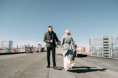 Sokaktaki binanın çatısında çekim düğün öncesi. Gülme, sarılma ve çalışan mutlu çift. Gülümse ve halkı yakışıklı görünüyor. günbatımı evleri ve sokakları