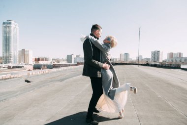 Sokaktaki binanın çatısında çekim düğün öncesi. Gülme, sarılma ve çalışan mutlu çift. Gülümse ve halkı yakışıklı görünüyor. günbatımı evleri ve sokakları