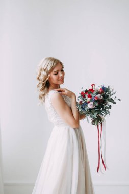 Parlak bir stüdyoda gelinlik içinde güzel bir gelin. Avrupa usulü düğün. Dekor ve buket elinde. Genç kız ayakta, oturuyor ve poz veriyor.