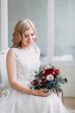 Parlak bir stüdyoda gelinlik içinde güzel bir gelin. Avrupa usulü düğün. Dekor ve buket elinde. Genç kız ayakta, oturuyor ve poz veriyor.