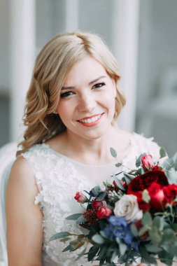 Parlak bir stüdyoda gelinlik içinde güzel bir gelin. Avrupa usulü düğün. Dekor ve buket elinde. Genç kız ayakta, oturuyor ve poz veriyor.