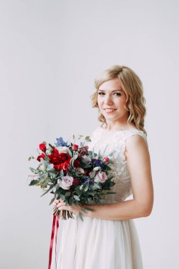 Parlak bir stüdyoda gelinlik içinde güzel bir gelin. Avrupa usulü düğün. Dekor ve buket elinde. Genç kız ayakta, oturuyor ve poz veriyor.