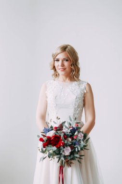 Parlak bir stüdyoda gelinlik içinde güzel bir gelin. Avrupa usulü düğün. Dekor ve buket elinde. Genç kız ayakta, oturuyor ve poz veriyor.