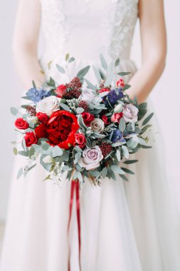 Parlak bir stüdyoda gelinlik içinde güzel bir gelin. Avrupa usulü düğün. Dekor ve buket elinde. Genç kız ayakta, oturuyor ve poz veriyor.