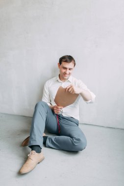 Doğal ışık ile yakışıklı genç damat Studio. Avrupa tarzı düğün fotoğraf çekimi. Adam oturan kat ve ayakta, yalan makinesini holding üzerinde gülümseyen