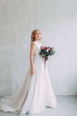 Parlak bir stüdyoda gelinlik içinde güzel bir gelin. Avrupa usulü düğün. Dekor ve buket elinde. Genç kız ayakta, oturuyor ve poz veriyor.