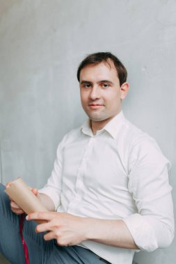 Doğal ışık ile yakışıklı genç damat Studio. Avrupa tarzı düğün fotoğraf çekimi. Adam oturan kat ve ayakta, yalan makinesini holding üzerinde gülümseyen