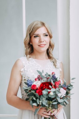 Parlak bir stüdyoda gelinlik içinde güzel bir gelin. Avrupa usulü düğün. Dekor ve buket elinde. Genç kız ayakta, oturuyor ve poz veriyor.