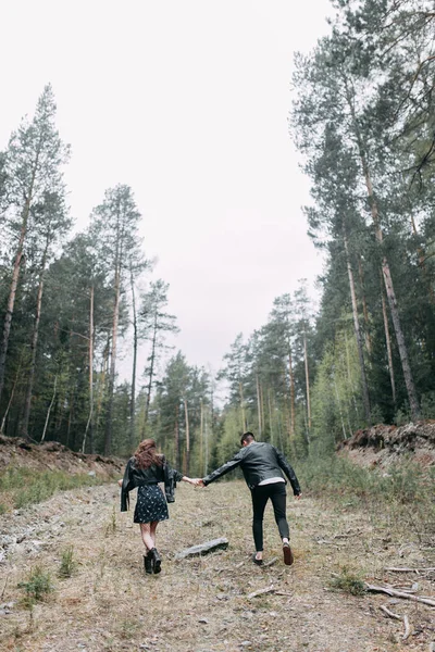 Young stylish couple in the forest, running around the Park and laughing. Modern people on a walk. Beautiful girl with tattoos. Loving young man and girl. mountain Park with pine forest