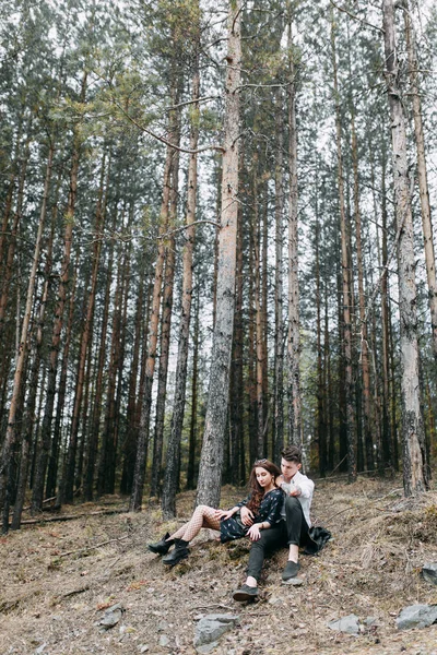 Young stylish couple in the forest, running around the Park and laughing. Modern people on a walk. Beautiful girl with tattoos. Loving young man and girl. mountain Park with pine forest