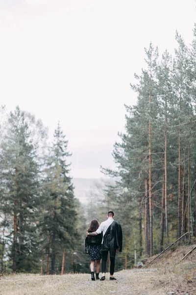 Young stylish couple in the forest, running around the Park and laughing. Modern people on a walk. Beautiful girl with tattoos. Loving young man and girl. mountain Park with pine forest