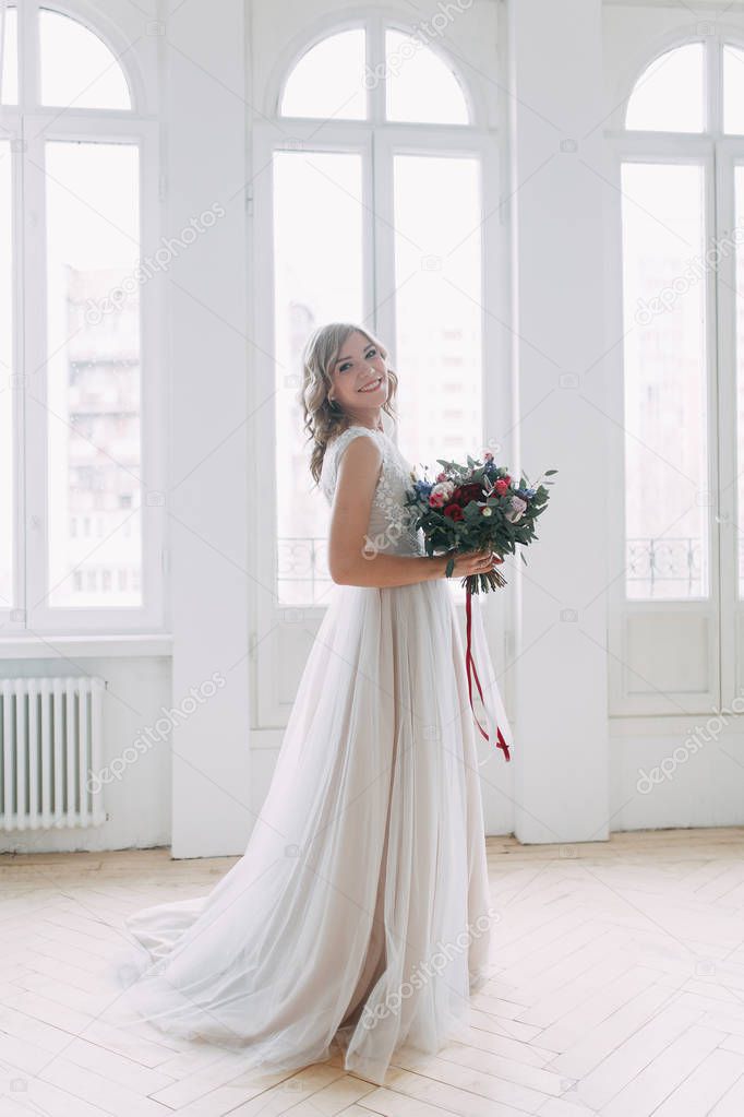Beautiful bride in a wedding dress in a bright stylish Studio. Wedding in European style. Decor and bouquet in hand. Young girl standing, sitting and posing
