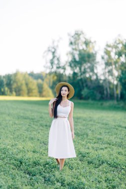 Bir şapka ve yaz elbise, alanın üzerinde yürüyen kız. Gülümseyen ve gülüyor, orman ve doğa güzel gün batımı. Beyaz elbise ve çavdar, alanları eğimli. Mutlu traveler, yaşam biçimi.