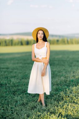 Bir şapka ve yaz elbise, alanın üzerinde yürüyen kız. Gülümseyen ve gülüyor, orman ve doğa güzel gün batımı. Beyaz elbise ve çavdar, alanları eğimli. Mutlu traveler, yaşam biçimi.