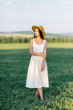 Bir şapka ve yaz elbise, alanın üzerinde yürüyen kız. Gülümseyen ve gülüyor, orman ve doğa güzel gün batımı. Beyaz elbise ve çavdar, alanları eğimli. Mutlu traveler, yaşam biçimi.