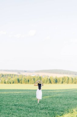 Bir şapka ve yaz elbise, alanın üzerinde yürüyen kız. Gülümseyen ve gülüyor, orman ve doğa güzel gün batımı. Beyaz elbise ve çavdar, alanları eğimli. Mutlu traveler, yaşam biçimi.