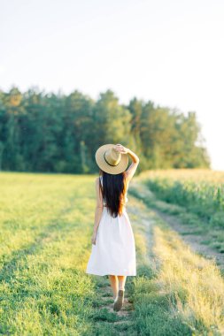 Bir şapka ve yaz elbise, alanın üzerinde yürüyen kız. Gülümseyen ve gülüyor, orman ve doğa güzel gün batımı. Beyaz elbise ve çavdar, alanları eğimli. Mutlu traveler, yaşam biçimi.
