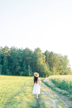 Bir şapka ve yaz elbise, alanın üzerinde yürüyen kız. Gülümseyen ve gülüyor, orman ve doğa güzel gün batımı. Beyaz elbise ve çavdar, alanları eğimli. Mutlu traveler, yaşam biçimi.