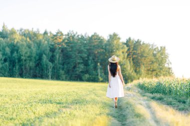 Bir şapka ve yaz elbise, alanın üzerinde yürüyen kız. Gülümseyen ve gülüyor, orman ve doğa güzel gün batımı. Beyaz elbise ve çavdar, alanları eğimli. Mutlu traveler, yaşam biçimi.