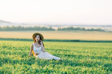 Bir şapka ve yaz elbise, alanın üzerinde yürüyen kız. Gülümseyen ve gülüyor, orman ve doğa güzel gün batımı. Beyaz elbise ve çavdar, alanları eğimli. Mutlu traveler, yaşam biçimi.