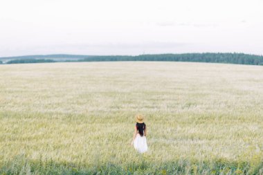 Bir şapka ve yaz elbise, alanın üzerinde yürüyen kız. Gülümseyen ve gülüyor, orman ve doğa güzel gün batımı. Beyaz elbise ve çavdar, alanları eğimli. Mutlu traveler, yaşam biçimi.