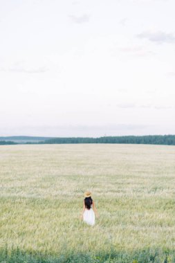 Bir şapka ve yaz elbise, alanın üzerinde yürüyen kız. Gülümseyen ve gülüyor, orman ve doğa güzel gün batımı. Beyaz elbise ve çavdar, alanları eğimli. Mutlu traveler, yaşam biçimi.