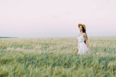 Bir şapka ve yaz elbise, alanın üzerinde yürüyen kız. Gülümseyen ve gülüyor, orman ve doğa güzel gün batımı. Beyaz elbise ve çavdar, alanları eğimli. Mutlu traveler, yaşam biçimi.