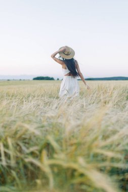 Bir şapka ve yaz elbise, alanın üzerinde yürüyen kız. Gülümseyen ve gülüyor, orman ve doğa güzel gün batımı. Beyaz elbise ve çavdar, alanları eğimli. Mutlu traveler, yaşam biçimi.