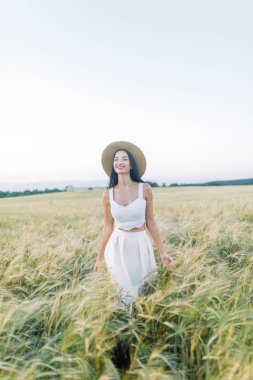 Bir şapka ve yaz elbise, alanın üzerinde yürüyen kız. Gülümseyen ve gülüyor, orman ve doğa güzel gün batımı. Beyaz elbise ve çavdar, alanları eğimli. Mutlu traveler, yaşam biçimi.