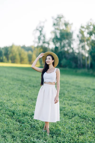 女孩走在田野上 在帽子和夏季礼服 微笑和欢笑 美丽的日落在森林和自然 白色礼服和黑麦 快乐的旅行者 生活方式 — 图库照片