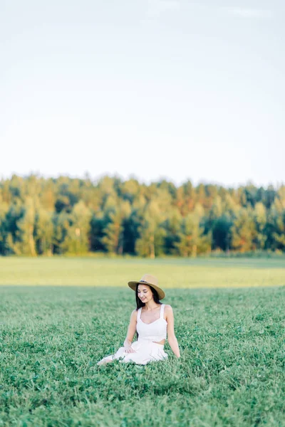 女孩走在田野上 在帽子和夏季礼服 微笑和欢笑 美丽的日落在森林和自然 白色礼服和黑麦 快乐的旅行者 生活方式 — 图库照片