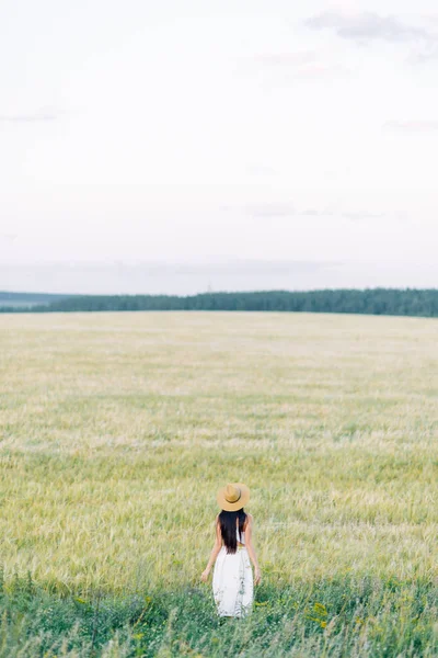 帽子と夏のドレスを着て フィールド上を歩く少女 笑顔し笑い 森林と自然の中の美しい夕日 白いドレスとライ 傾斜フィールド 幸せな旅行者 ライフ スタイル — ストック写真