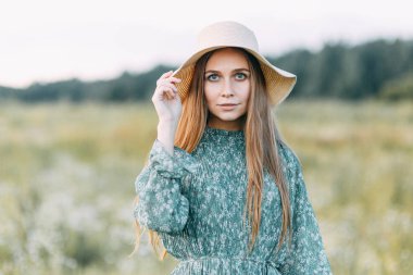 Güzel Rus kız bir şapka ve yaz elbise, çim sahada bel yürüme. Gülümseyen otlar, toplama mutlu traveler. Ormanda günbatımı.